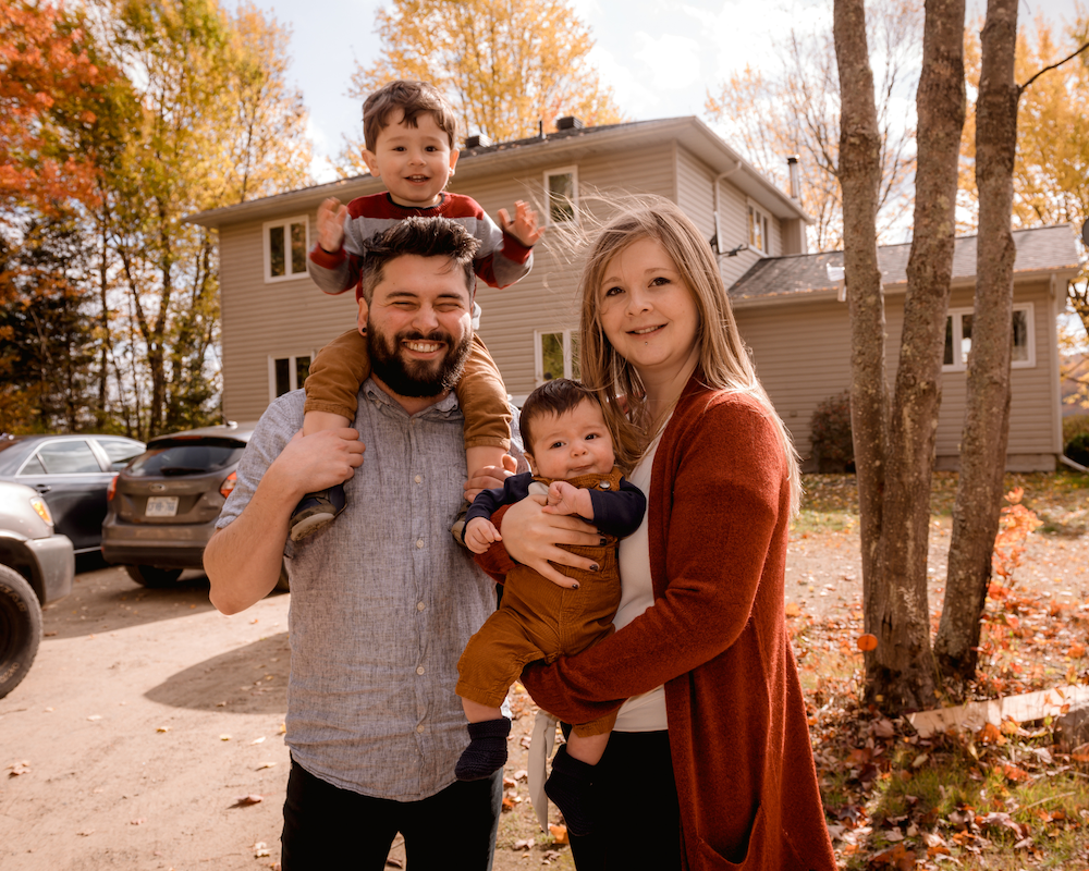 family picture in front of house with dad holding older brother around his neck and mom holding baby brother